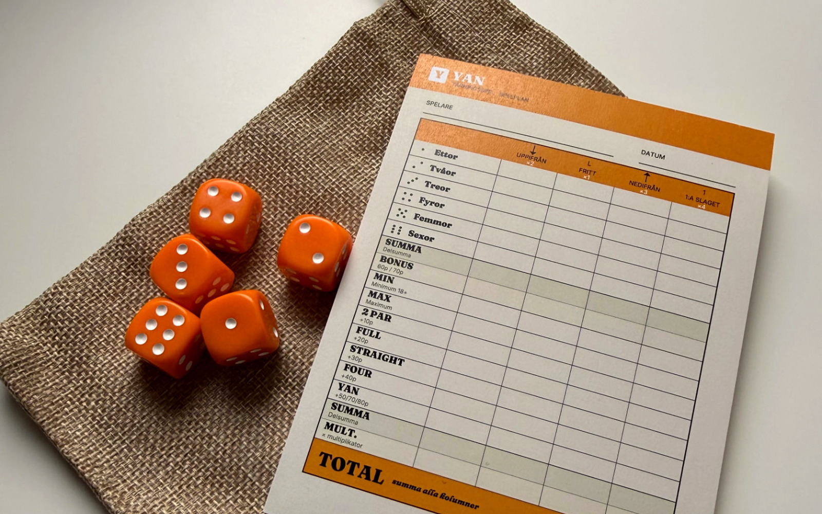 YAN-spelplan med orangea tärningar och jutepåse